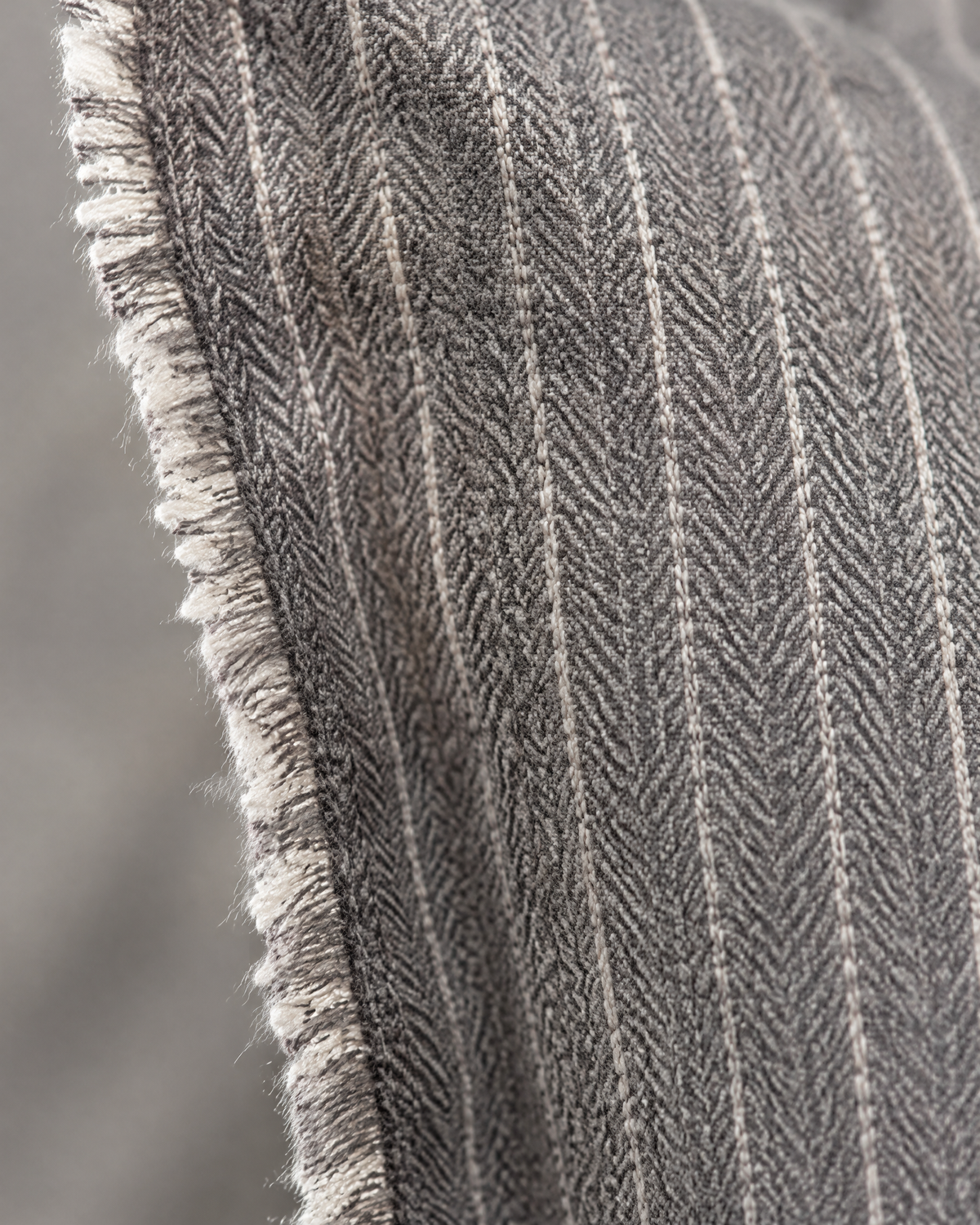 Macro close-up of the grey pinstripe, ivory stitched pinstripes on grey herringbone with a frayed fringe edge