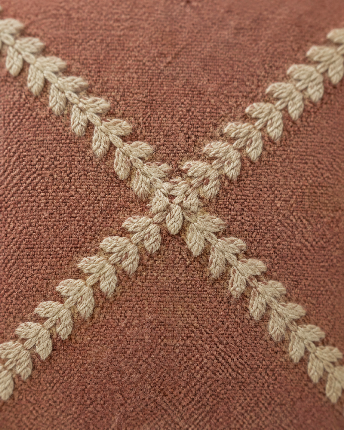 Macro close-up of the terracotta trellis lumbar, sand feather-stitch lines crossing on dusty terracotta cloth