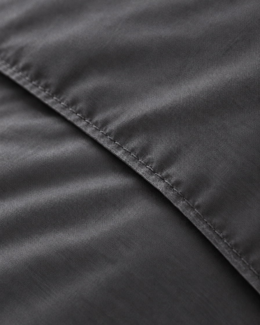 Macro of the stitched hem on a Charcoal Grey silky cotton duvet cover, showing the grey sateen weave and sheen.