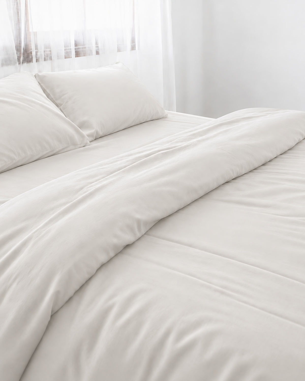 Milky White silky cotton duvet cover, white 300 TC cotton sateen, turned back on a bed by a white sheer curtain