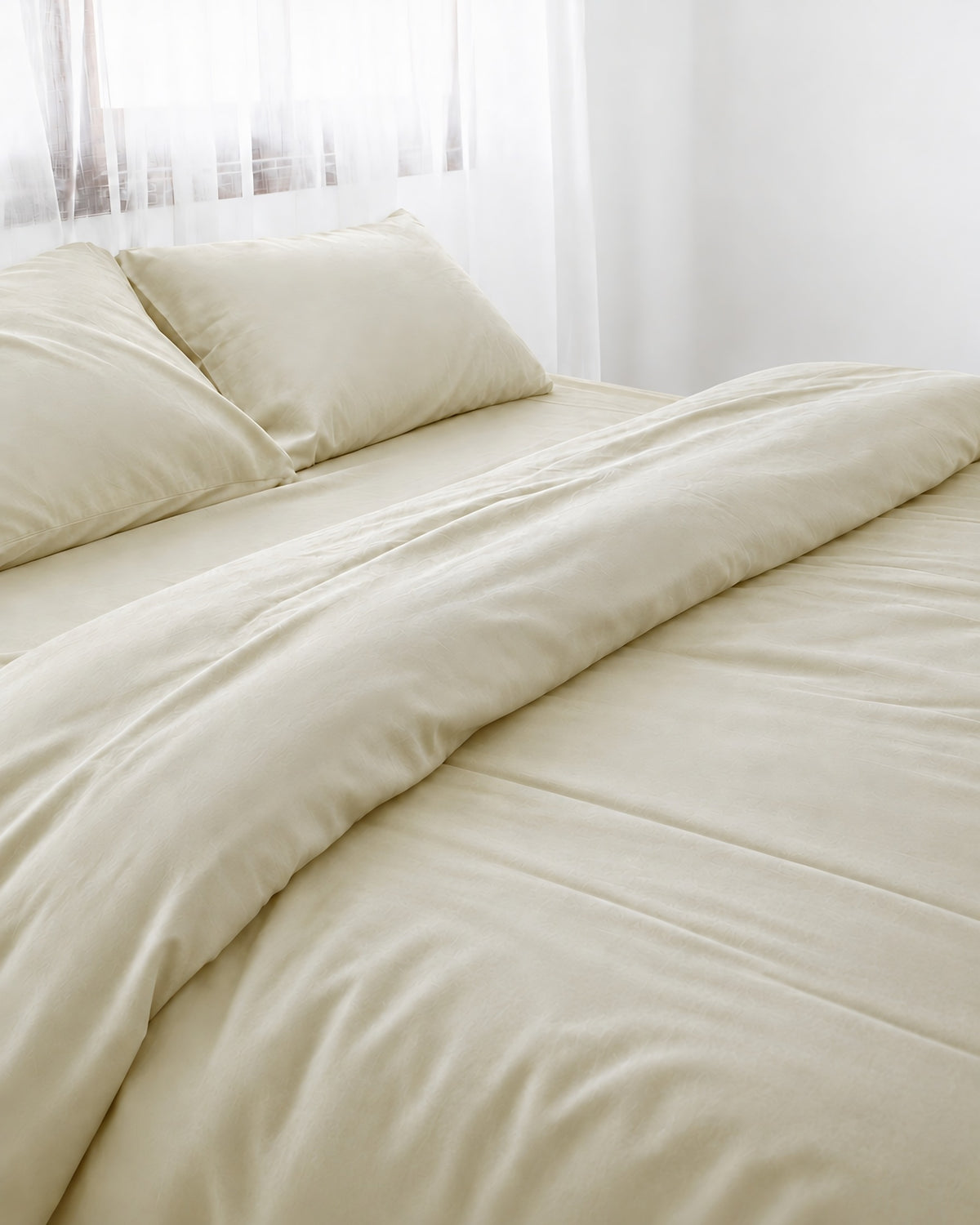 Vanilla silky cotton duvet cover, cream 300 TC cotton sateen, turned back on a bed by a white sheer curtain