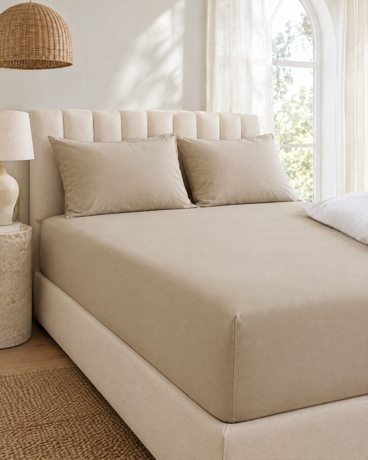 Beige plain cotton percale fitted sheet on a made bed in a bright bedroom