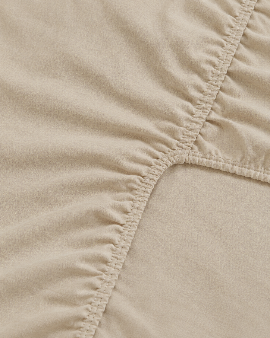 Close-up of elasticated corner and stitched edge of the fitted sheet in Cream Plain Cotton
