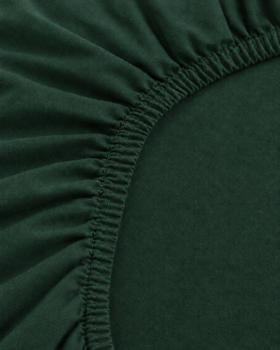 Close-up of the elasticated corner of a Forest Green plain cotton fitted sheet in bottle green