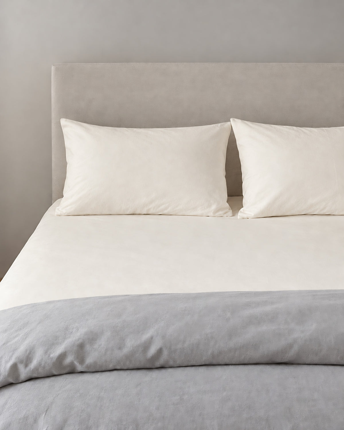 Off White plain cotton fitted sheet and pillowcases in warm ivory, grey duvet folded at the foot