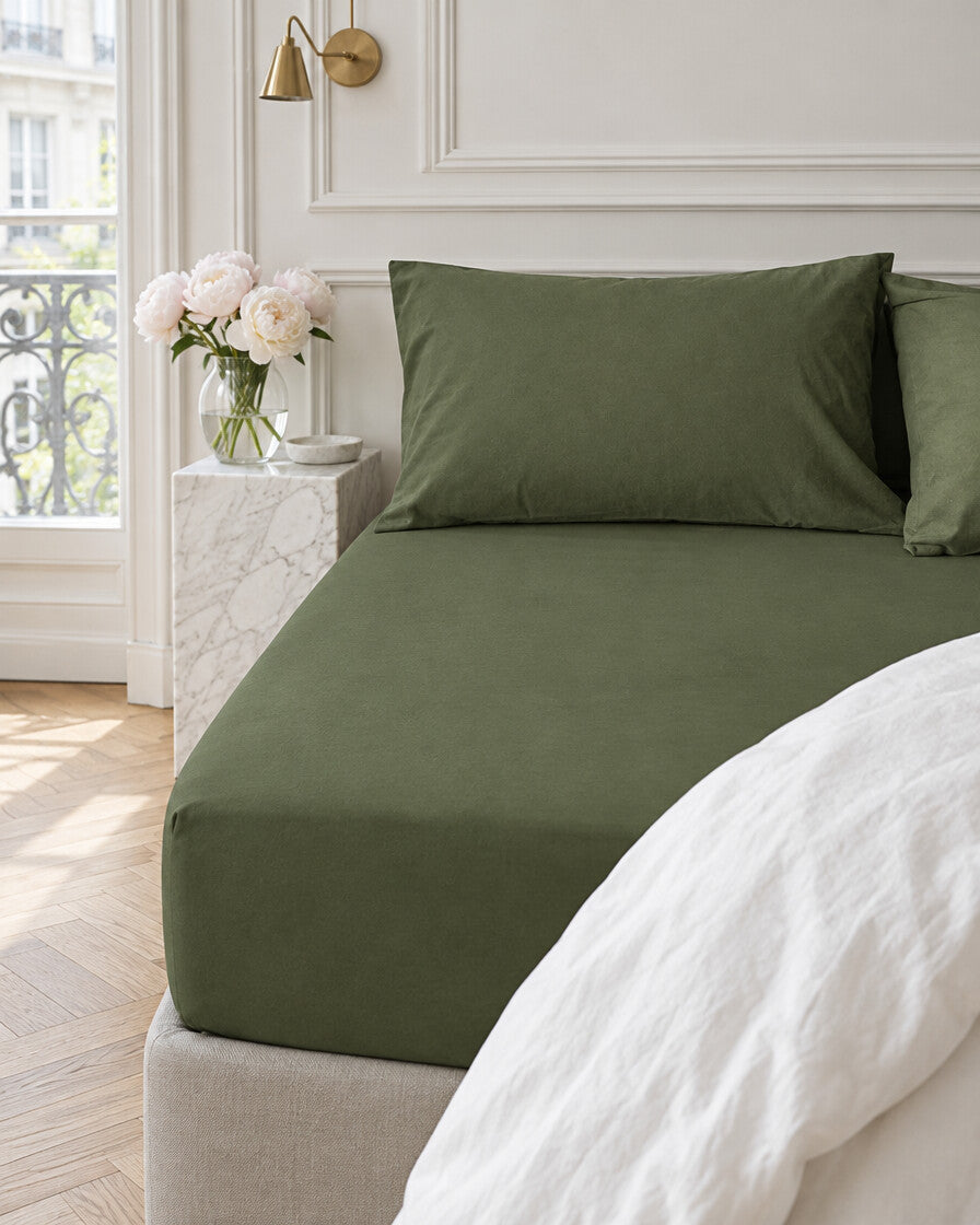 Olive green plain cotton fitted sheet in a Parisian bedroom with panelled walls and fresh peonies