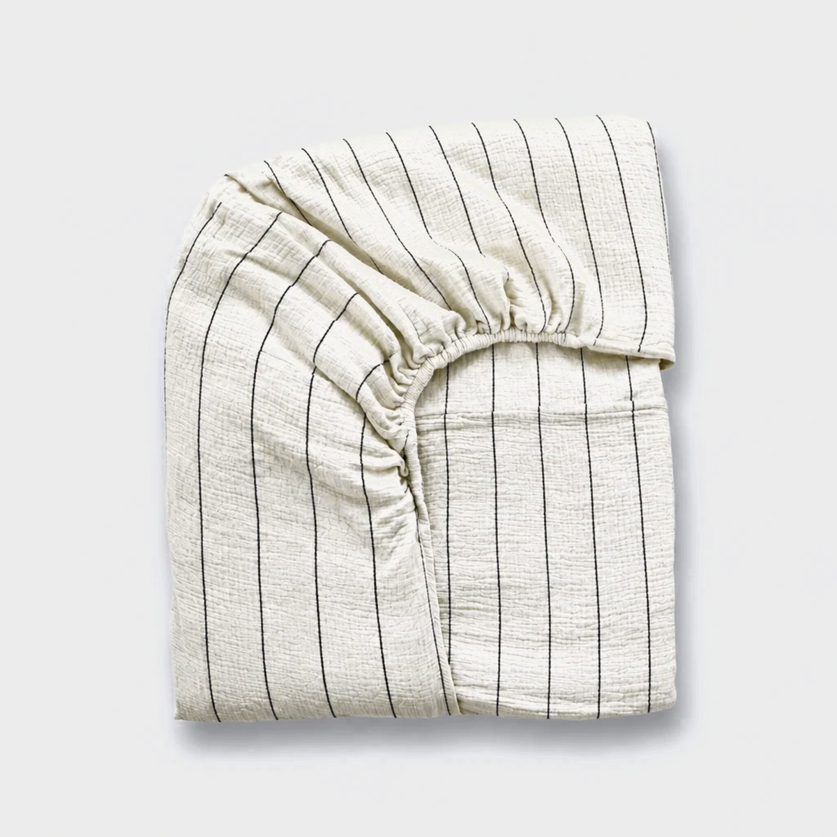 Folded cloud cotton fitted sheet with Black Pinstripe on off-white crinkled muslin, elastic corner visible.