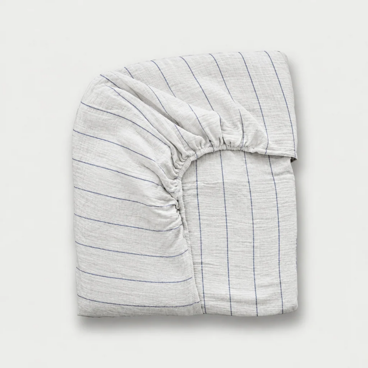 Folded cloud cotton fitted sheet with fine Blue Pinstripe on off-white crinkled muslin, plain background.