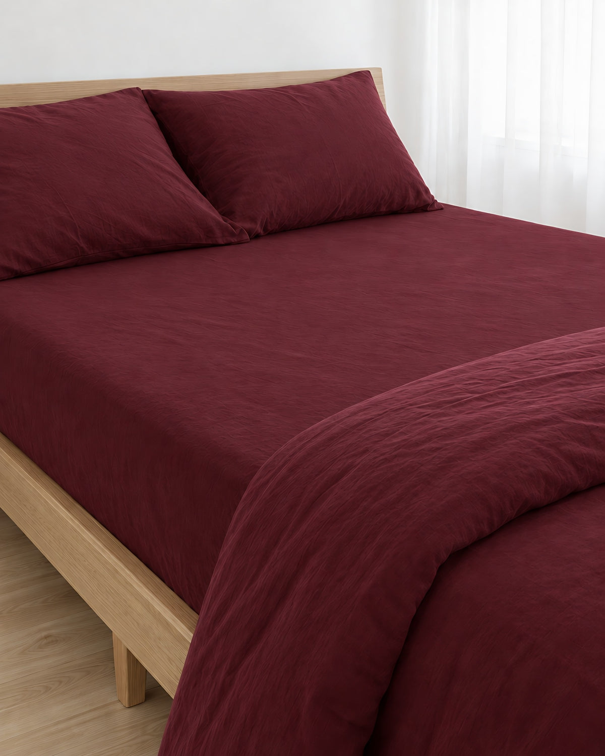 Burgundy Red plain cotton fitted sheet pulled taut over a mattress on an oak bed with matching pillows