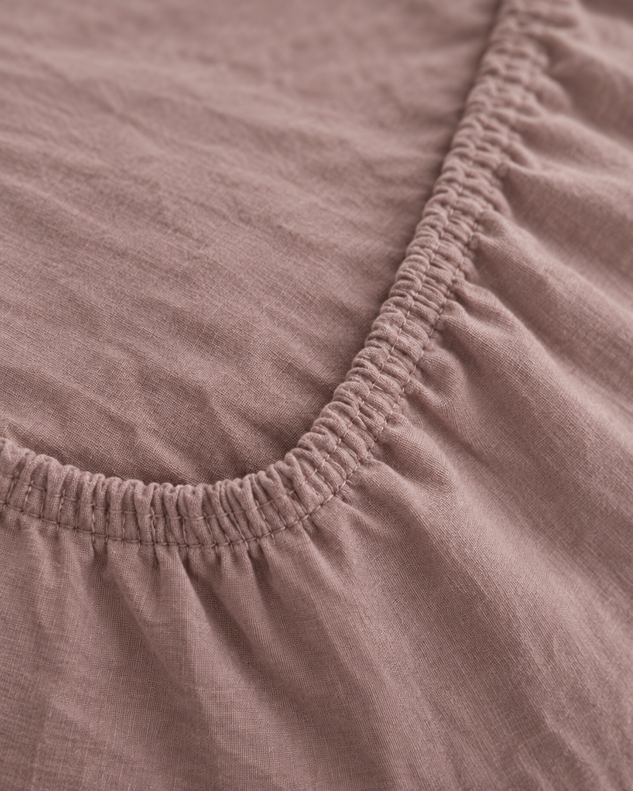 Macro of the gathered elastic corner of a Dust Pink plain cotton fitted sheet.