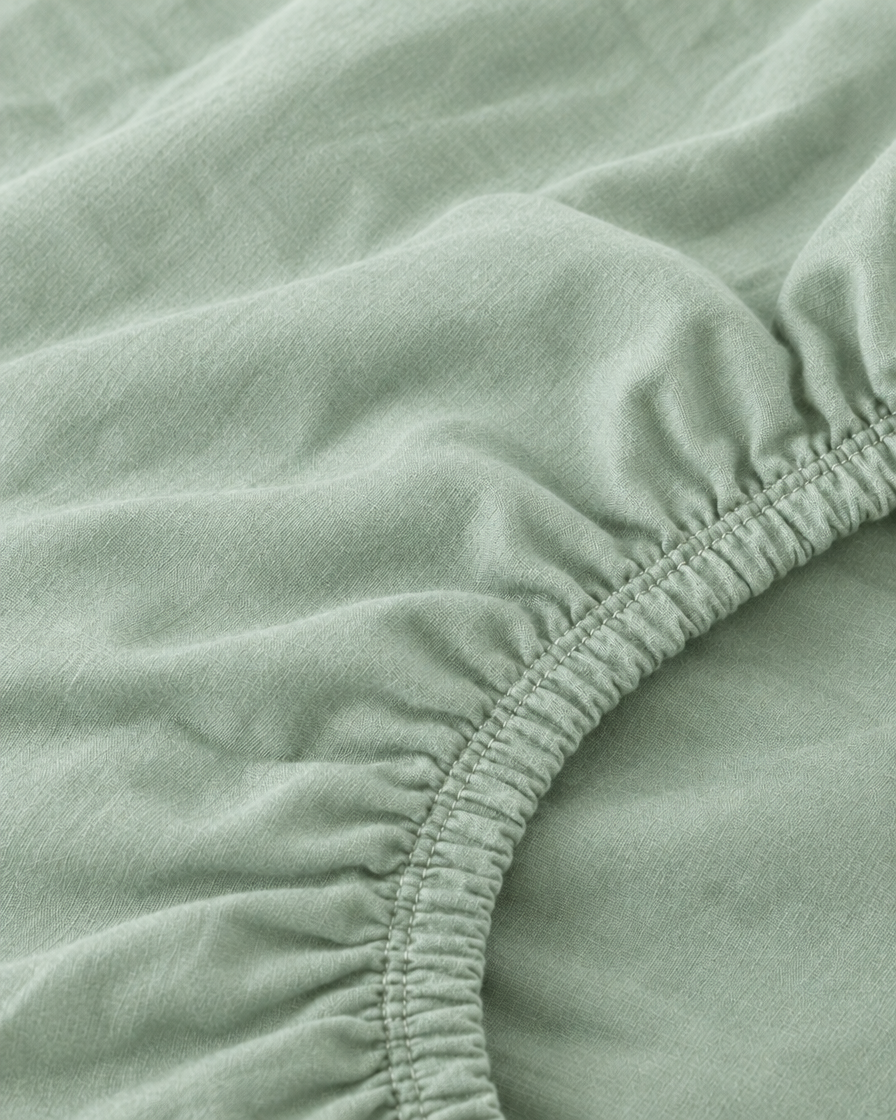 Macro of the gathered elastic corner of a Mint Green plain cotton fitted sheet.