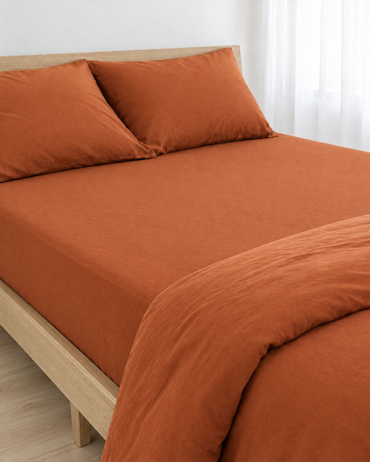 Terracotta plain cotton fitted sheet pulled taut over a mattress on an oak bed, with matching pillows and a folded duvet.