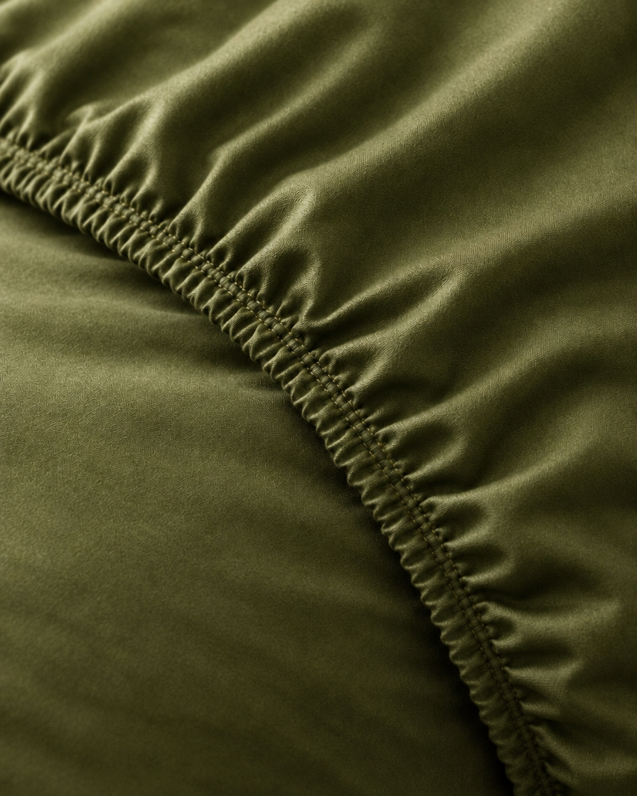 Macro of the gathered elastic corner of a Juniper Green silky cotton fitted sheet.