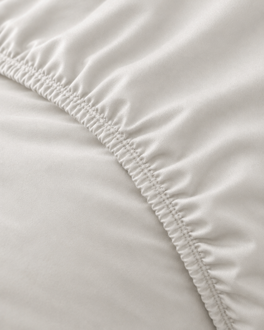 Macro of the gathered elastic corner of a Milky White silky cotton fitted sheet in white cotton sateen.