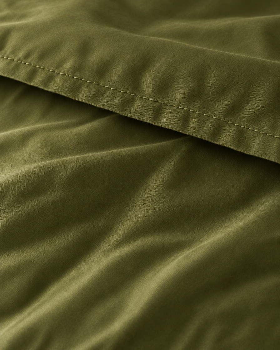 Macro of the stitched hem on a Juniper Green silky cotton flat sheet, showing the olive green sateen sheen.