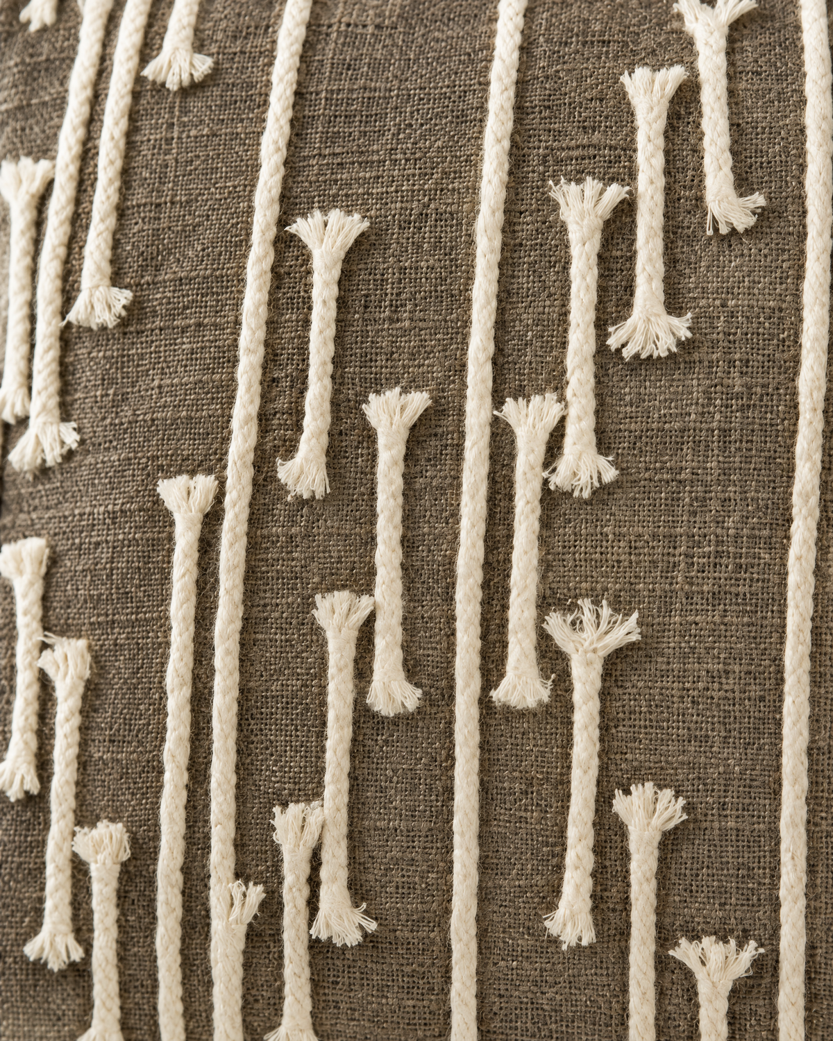 Macro close-up of thick ivory cord in tall reed lines with frayed tufted ends on the cocoa slub weave