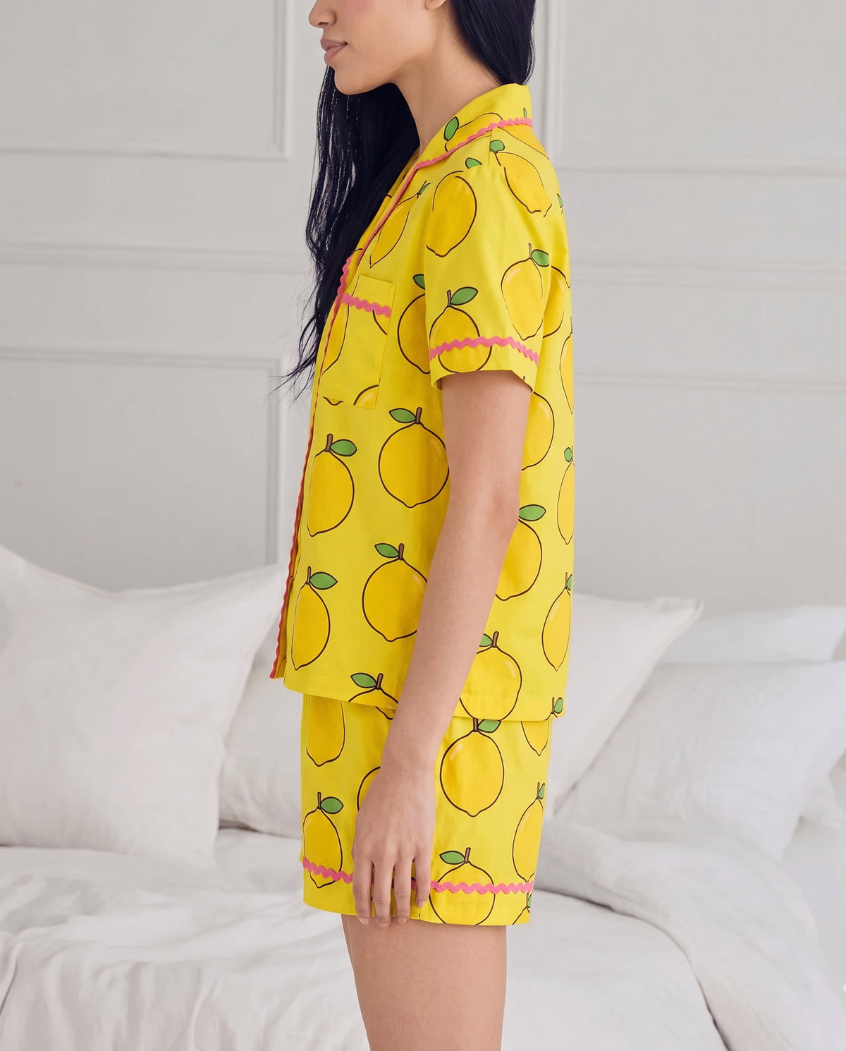 Ripe Lemon cotton pyjama set worn seated on a white bed.