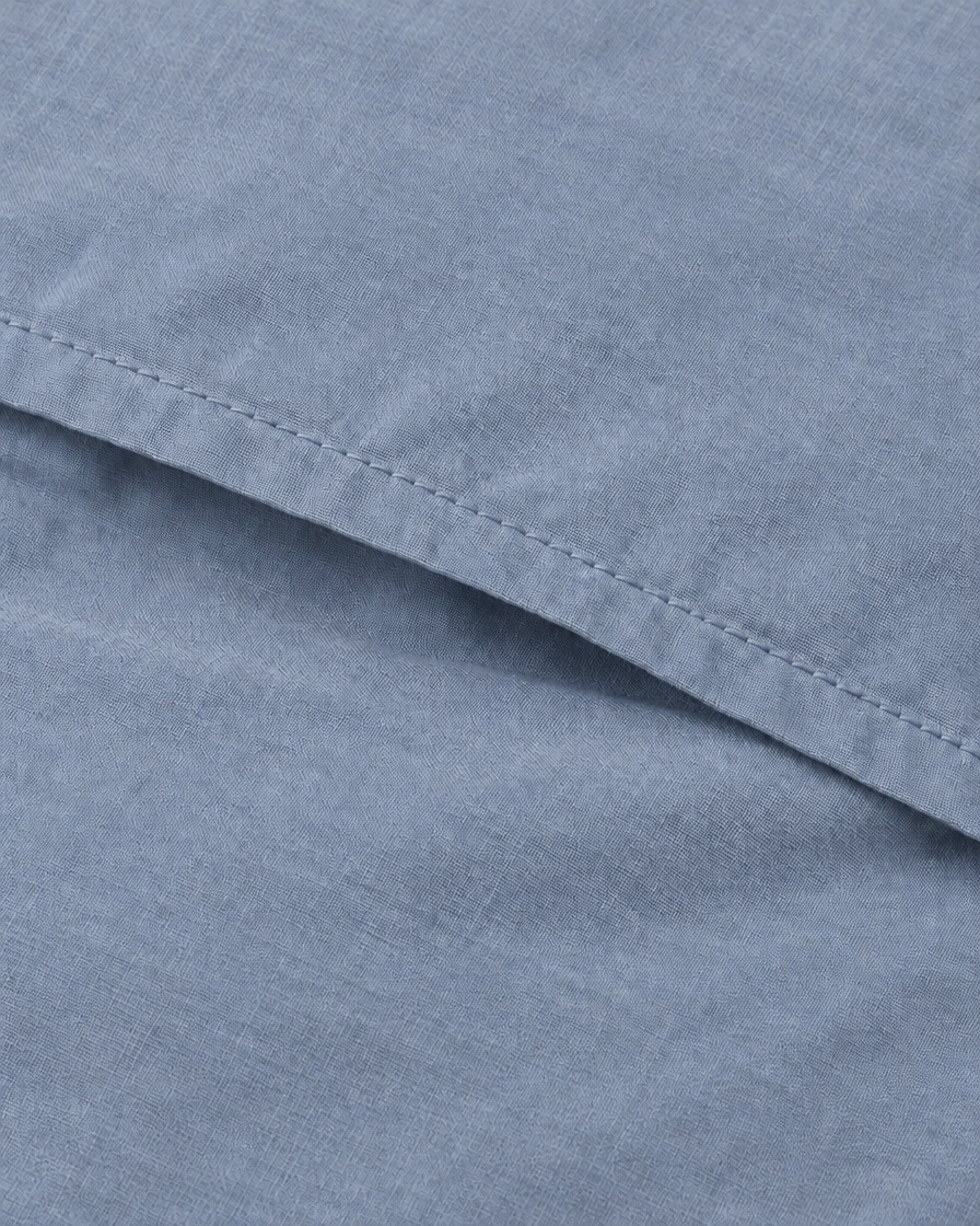 Close-up of the stitched envelope hem of a Light Jeans plain cotton pillowcase in greyed denim blue