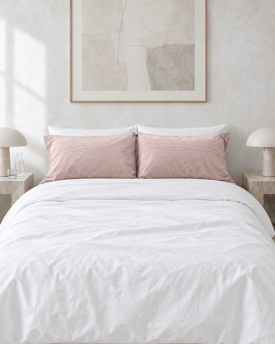 Pale pink plain cotton pillowcases on a white made bed against a limewashed plaster wall