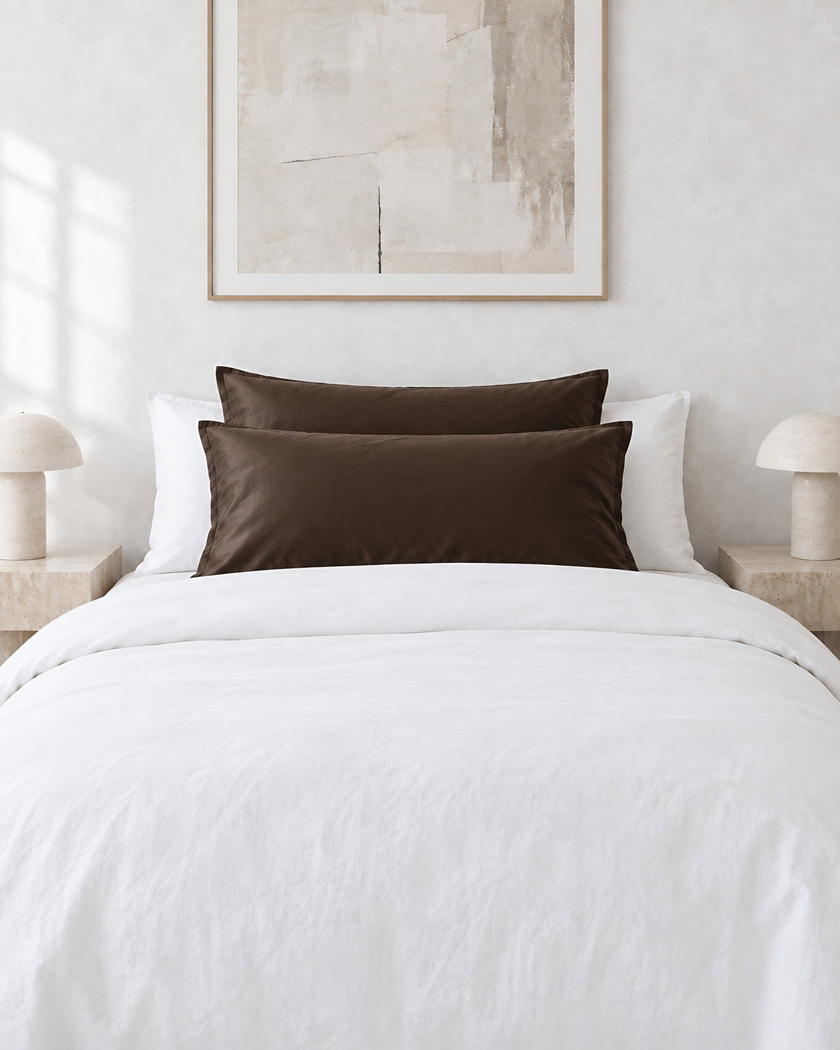 Chocolate silky cotton pillowcases on pillows against a white bed between bedside lamps