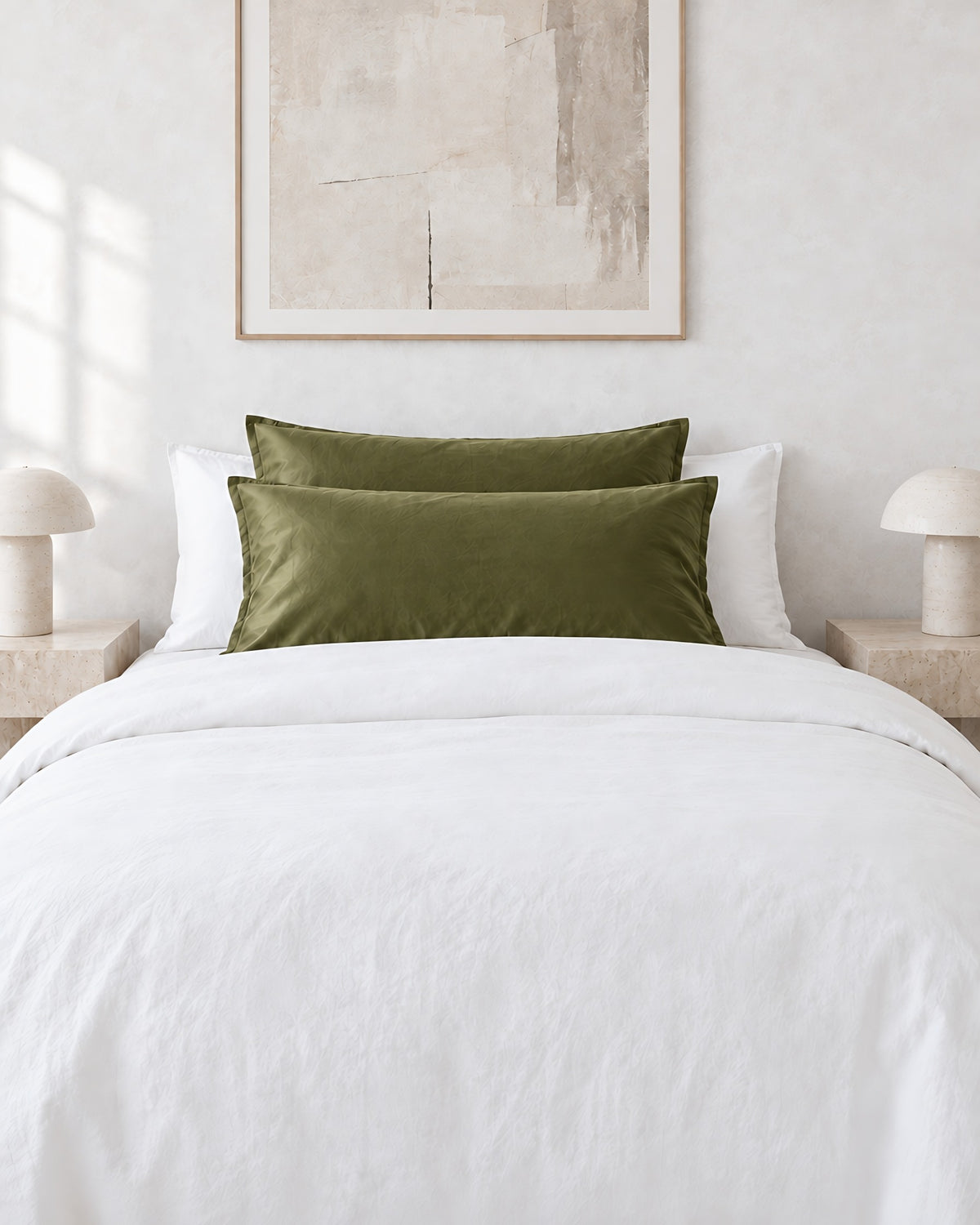 Juniper Green silky cotton pillowcases on pillows against a white bed between bedside lamps
