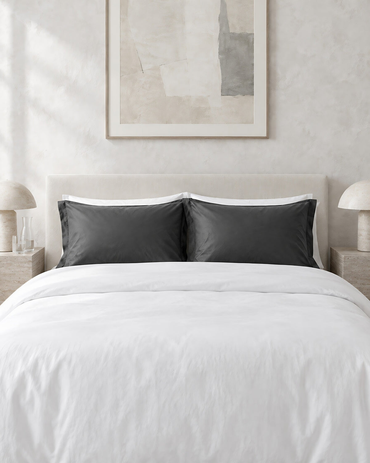 Charcoal Grey silky cotton pillowcases against a limewashed plaster wall between travertine bedside tables