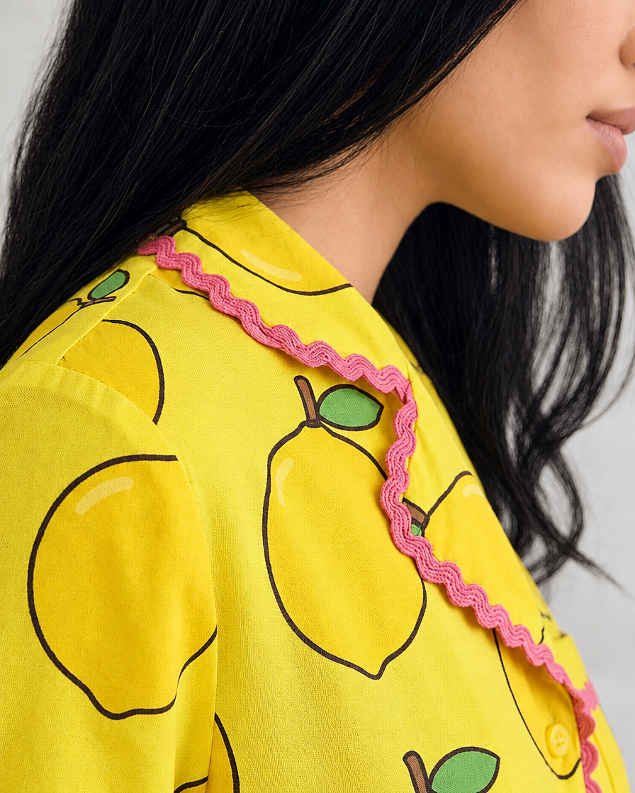 Close-up of the Ripe Lemon pyjama top's collar with pink ric-rac edging and large lemon print, worn by a woman