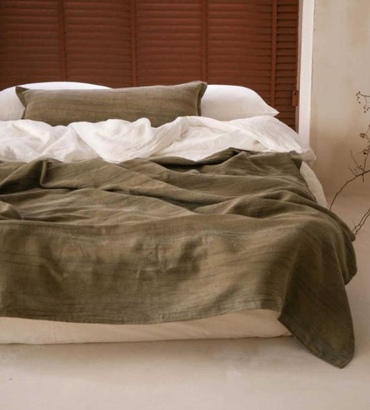Moss green washed linen cotton throw across the foot of a bed, a light summer throw
