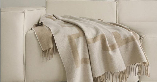 Camel lambswool throw with a key-pattern border draped over a cream sofa arm