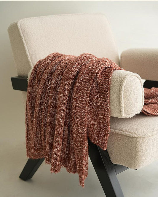 Rust cotton blend chunky knitted throw draped over a cream armchair