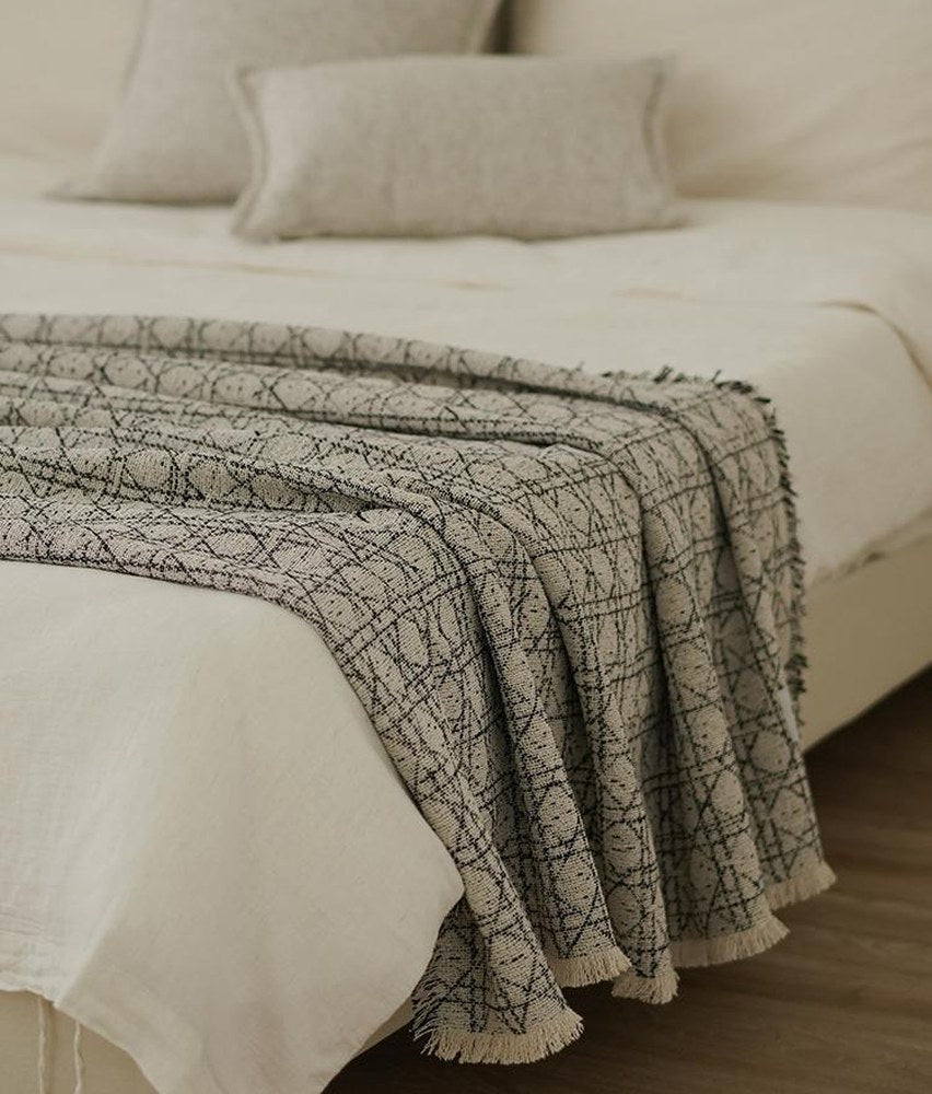Stone and black vine jacquard throw folded across the foot of a made bed