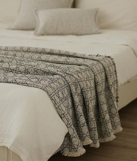 Stone and black vine jacquard throw folded across the foot of a made bed