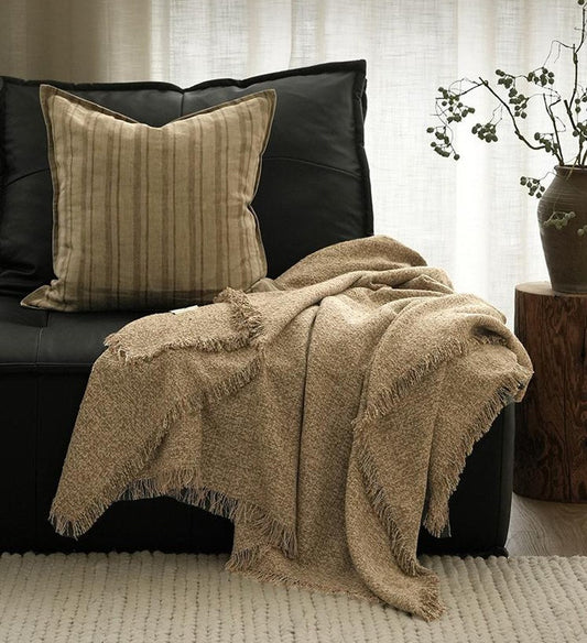 Toffee nubbly fringed throw arranged with cushions on a dark sofa