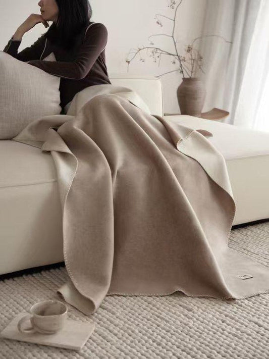 Woman on a cream sofa under an oat pure wool throw with a fine striped edge