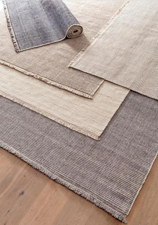 Stack of heathered wool loop-pile rugs, ivory to charcoal, for a rug under a bed