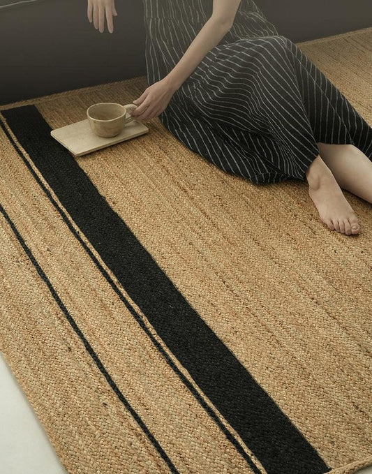 Natural jute rug with a black band border as a woman sets down a tray