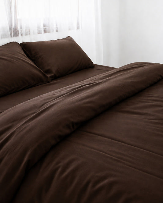 Chocolate silky cotton sateen duvet cover with one corner turned back on a bed by a white sheer curtain