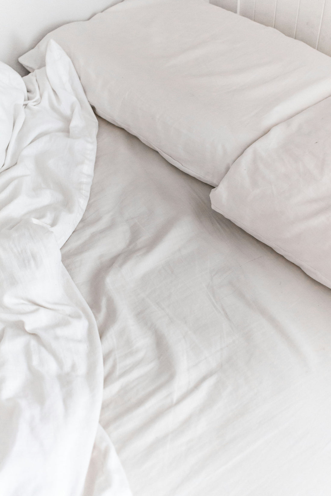 White cotton bedding and a pillow seen from above against a painted wooden headboard.
