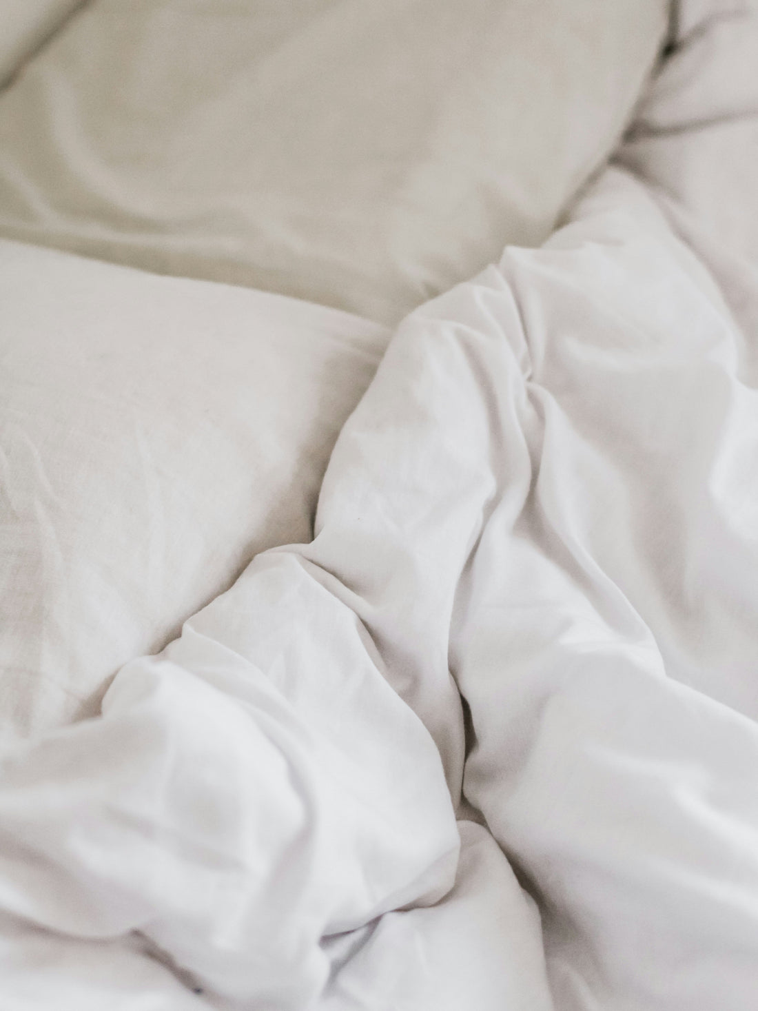 Close view of white cotton duvet folds beside an oatmeal pillow.