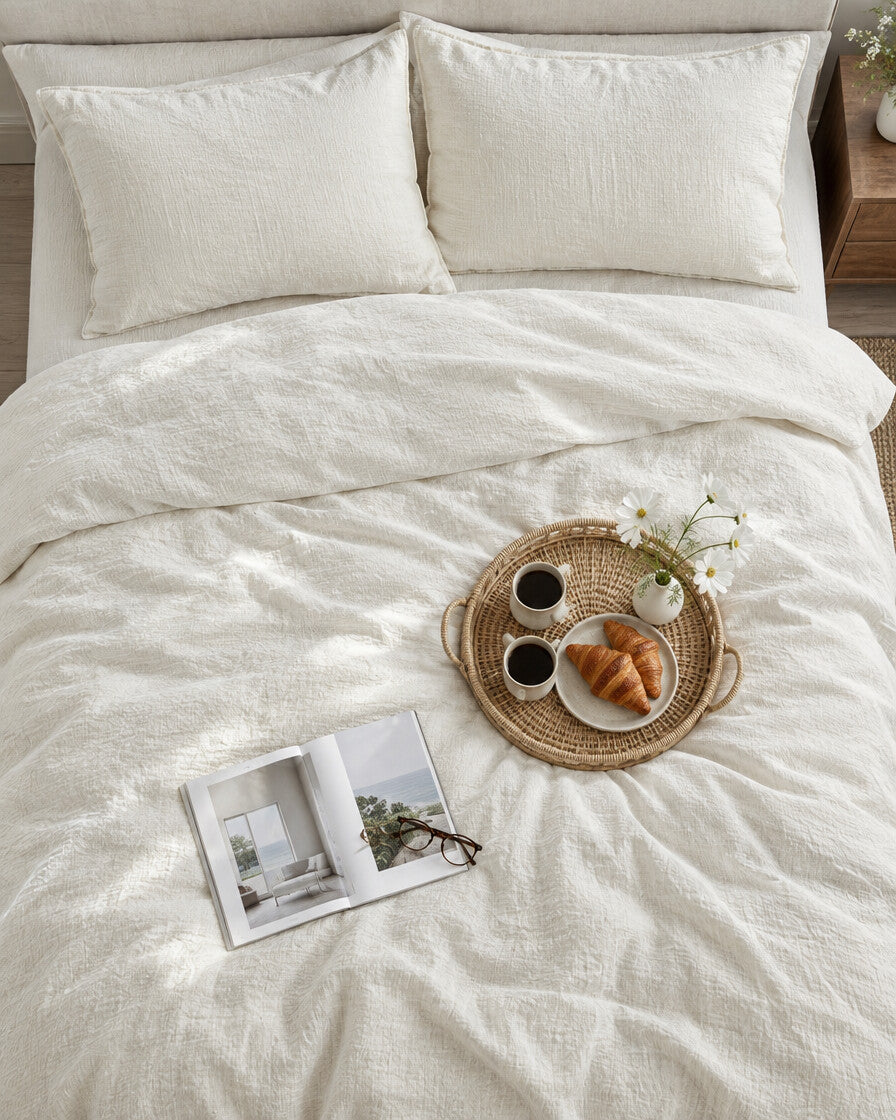 Off-white cloud cotton bedding set seen from above with a breakfast tray of coffee and croissants