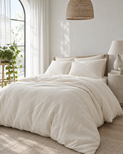 Off-white cloud cotton bedding set beneath an arched window with a trailing pothos and rattan pendant