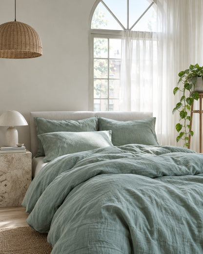 Sage green cloud cotton bedding set beneath an arched window with a trailing pothos and rattan pendant