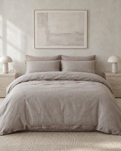 Greige cloud cotton bedding set against a limewashed plaster wall between travertine bedside tables