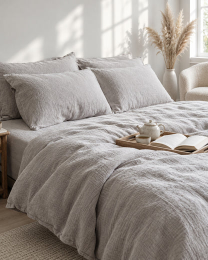 Warm grey cloud cotton bedding set with a tea tray and open book, a boucle armchair in the corner