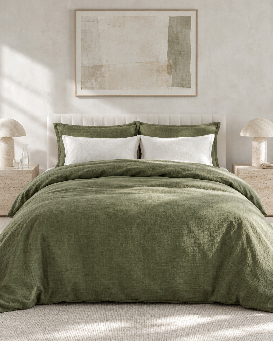 Olive green cloud cotton bedding set against a limewashed plaster wall between travertine bedside tables
