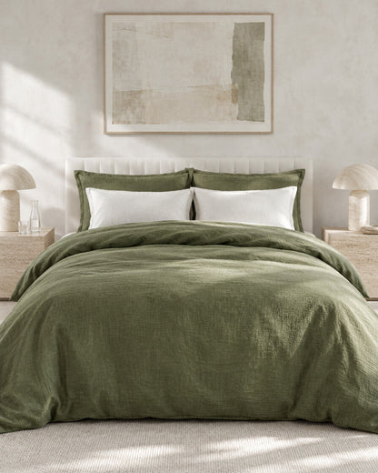 Olive green cloud cotton bedding set against a limewashed plaster wall between travertine bedside tables