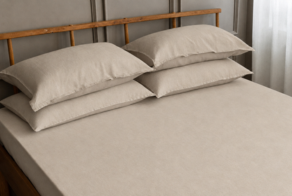 Natural French linen fitted sheet and four pillows on a wooden-framed bed.
