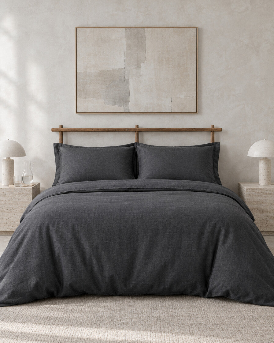 Charcoal French linen bedding set against a limewashed plaster wall between travertine bedside tables