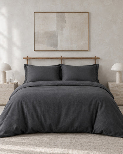 Charcoal French linen bedding set against a limewashed plaster wall between travertine bedside tables