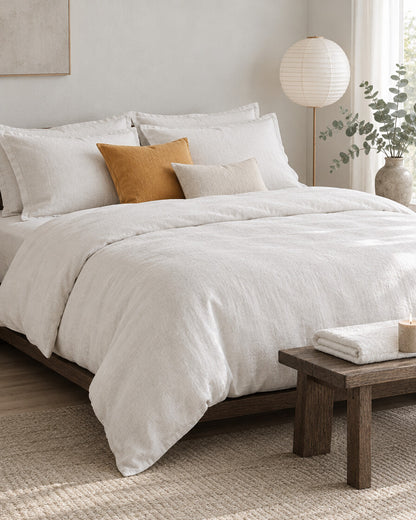 White French linen bedding set with mustard and cream cushions in a calm Japandi bedroom on a low dark-oak bed
